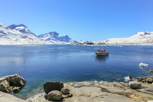 Boat anchored in the lagoon and Qoornoq former fishermen village in the middle of Nuuk fjord, Greenland