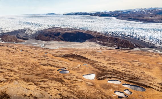 Greenlandic ice sheet melting glacier into river with tundra aerial view, near Kangerlussuaq, Greenland