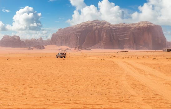 Orange sands and cliffs of Wadi Rum desert with tourist car in the background, Jordan