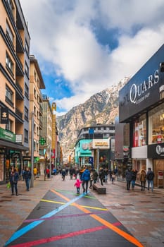 Andorra la Vella, Andorra, Jan 2020 People walking and shopping on promenade with shops and restaurants, Pyrenees Mountains in background