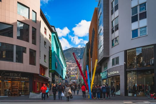 Andorra la Vella, Andorra, Jan 2020 People walking and shopping on promenade, street with shops and restaurants, Pyrenees Mountain range in background