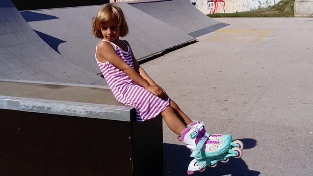 Sremska Mitrovica, Serbia, September 12, 2020. The girl is rollerblading on the asphalt. A 7-year-old child in a striped white and pink dress rides on roller skates on the playground