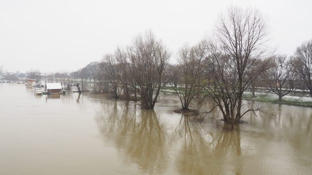 Macvanska Mitrovica, Serbia, 01/27/2023 The bridge over the Sava River. Flooding after heavy rains and snowmelt. A swift flow of muddy water. Trees, boats and piers in the water. Machva in winter