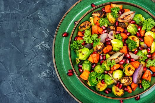 Salad with grilled brussels sprouts, grilled carrots, decorated with greens and pomegranate. Copy space, vegan menu