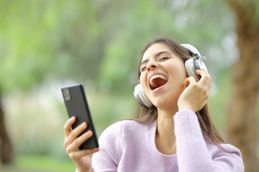Happy teen singing in a park listening music with headphones and phone