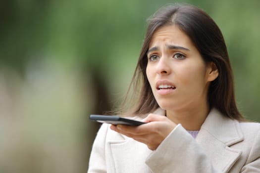 Worried woman dictating message on cell phone in a park in winter