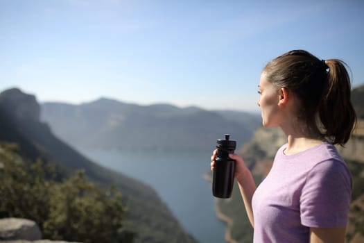 Sportswoman holding drink watching landscape in nature