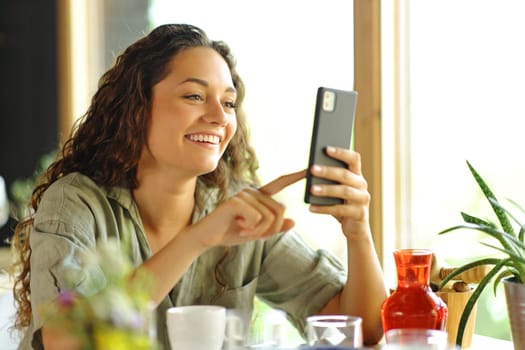 Happy woman smiling using phone in a restaurant