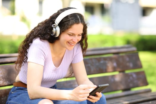 Woman with headphones watching content on smartphone siting on a bench