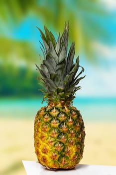 A beautiful fresh fruity pineapple on a table over abstract blurred tropical sandy beach background. Summer holiday and health concept.