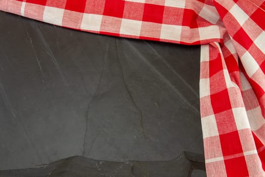Red white checkered tablecloth on massive slate plate or black stone background texture. Template for design menu card and blackboard. Copy space. Top view.