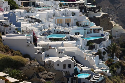 Oia, Santorini, Greece - July 3, 2021: Whitewashed houses with terraces and pools and a beautiful view in Oia on Santorini island, Greece