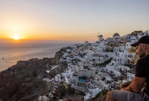 Oia, Santorini, Greece - June 28, 2021: Whitewashed houses and windmills in Oia in warm rays of sunset on Santorini island. Greece