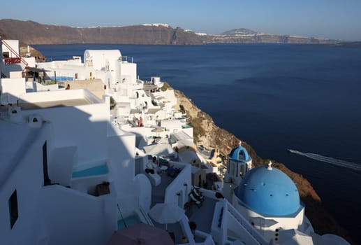 Oia, Santorini, Greece - June 28, 2021: View from viewpoint of Oia village with blue dome of  greek orthodox Christian church and traditional whitewashed greek architecture.  Santorini, Greece