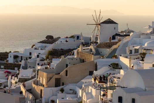 Oia, Santorini, Greece - June 28, 2021: Whitewashed houses and windmills in Oia in warm rays of sunset on Santorini island. Greece