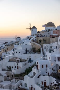 Oia, Santorini, Greece - June 28, 2021: Whitewashed houses and windmills in Oia in warm rays of sunset on Santorini island. Greece