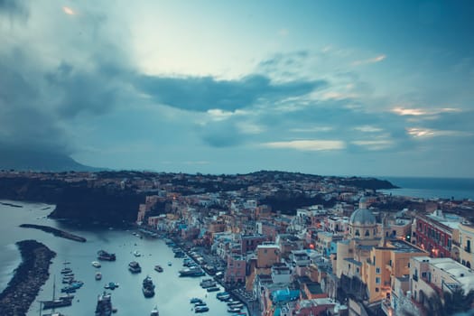 View of the Port of Corricella with lots of colorful houses after sunset in Procida Island, Italy.