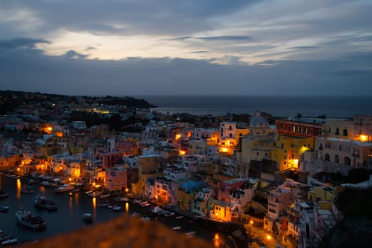 View of the Port of Corricella with lots of colorful houses after sunset in Procida Island, Italy.