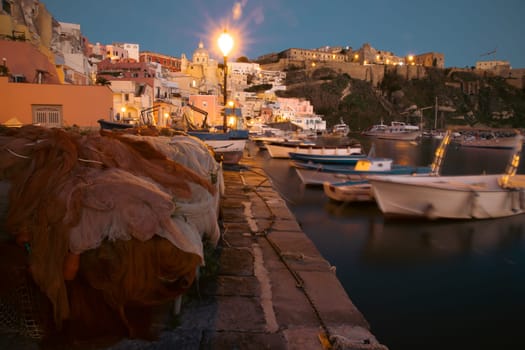 Fishing nets the Port of Corricella with lots of colorful houses after sunset in Procida Island, Italy.
