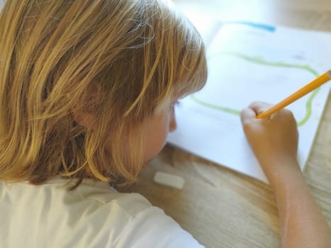 A 6 or 7 year old girl draws in a book. The child does his homework. Blond hair and pink-rimmed glasses. Training and education concept.