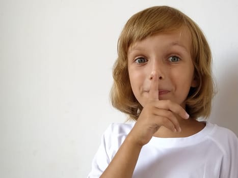 Silence gesture. The finger is near the mouth. The girl on a white background shows a gesture of keeping silence. Child of 7 years old with blond hair. Caucasian type. Copy space. Place for text.