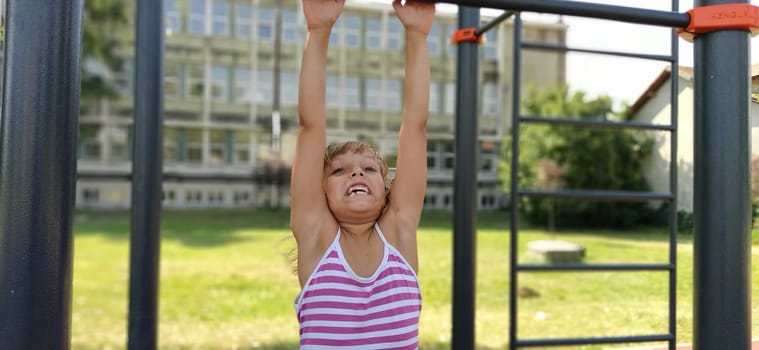 Sremska Mitrovica, Serbia, September 15, 2020 A child in a striped dress hangs on a metal bar and tries to pull up on his arms. Sports or playground. Outdoor exercise