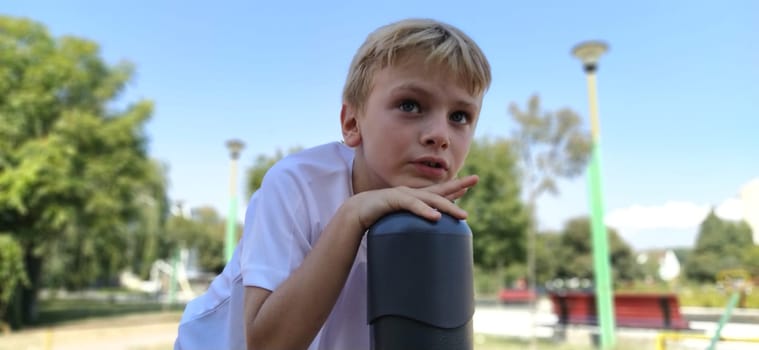 Pensive boy on the playground. The child lingered on top of the metal structure, and thought. Boy with blond hair.