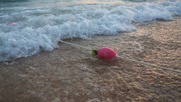 Buoys on a rope near sea water. The buoys are pink restraints to alert people to the depth of the water. Rescue of the drowning. Delimiting a place on a sandy beach between hotels. Wave with bubbles