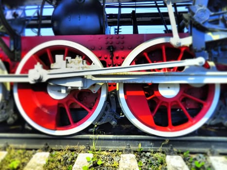 Retro vintage wheels of a locomotive or train close up. Red large heavy metal wheels with piston guiding mechanisms. Locomotive of the 19th - 20th centuries with a steam engine. Bright vivid photo.