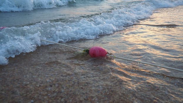 Buoys on a rope near sea water. The buoys are pink restraints to alert people to the depth of the water. Rescue of the drowning. Delimiting a place on a sandy beach between hotels. Wave with bubbles