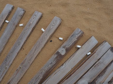 Wooden footbridge on a sandy beach. Uneven, damp wooden planks held together. The edge of the beach season at the hotel. No people, copy space. Equipped sandy beach after a storm or cyclone. Tourism.