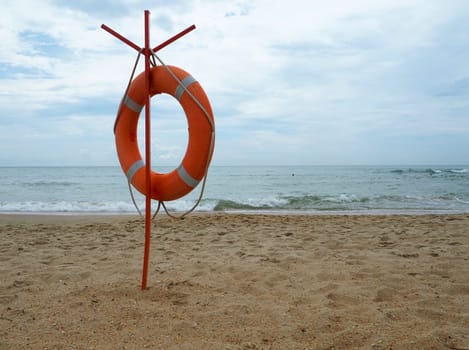 Lifebuoy on a sandy beach. Orange circle on a pole to rescue people drowning in the sea. Rescue point on the shore. Sky and sea in the background