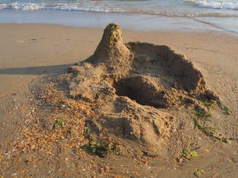 a palace or a house made of sand on a sandy beach. Excavated pit, elevation and seaweed on the roof of the house. Child's vacation at sea. Imagination and fantasy in the creativity of children.