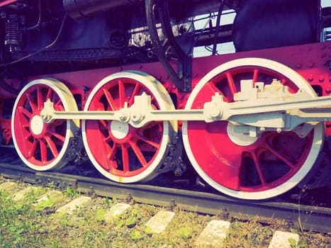 Retro vintage wheels of a locomotive or train close up. Red large heavy metal wheels with piston guiding mechanisms. Locomotive of the 19th - 20th centuries with a steam engine. Retro style.