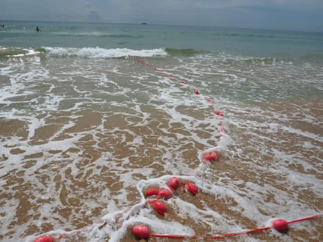 Buoys on a rope in sea water. The lifebuoys are pink restraints to alert people to the depth of the water. Rescue of the drowning. Delimiting a place on a sandy beach between hotels. Wave with bubbles