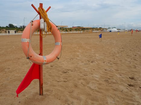 Anapa, Russia, August 10, 2021 Lifebuoy with a red flag on a sandy beach. Orange lifebuoy on a pole to rescue people drowning in the sea. Rescue point on the shore. Stormy weather on the Black Sea.
