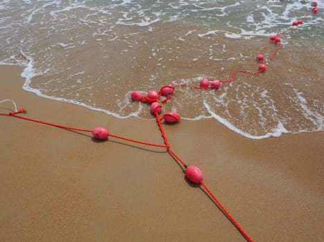 Buoys on a rope in sea water. The lifebuoys are pink restraints to alert people to the depth of the water. Rescue of the drowning. Delimiting a place on a sandy beach between hotels. Wave with bubbles