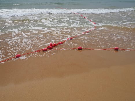 Buoys on a rope in sea water. The lifebuoys are pink restraints to alert people to the depth of the water. Rescue of the drowning. Delimiting a place on a sandy beach between hotels. Wave with bubbles.