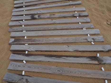 Wooden footbridge on a sandy beach. Uneven, damp wooden planks held together. The edge of the beach season at the hotel. No people, copy space. Equipped sandy beach after a storm or cyclone. Tourism.