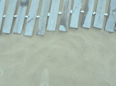 Wooden footbridge on a sandy beach. Uneven, damp wooden planks held together. The edge of the beach season at the hotel. No people, copy space. Equipped sandy beach after a storm or cyclone. Tourism.