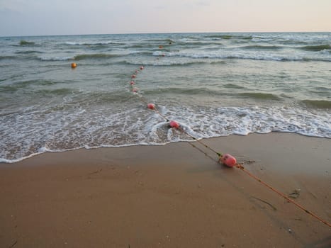 Buoys on a rope near sea water. The buoys are pink restraints to alert people to the depth of the water. Rescue of the drowning. Delimiting a place on a sandy beach between hotels. Wave with bubbles.