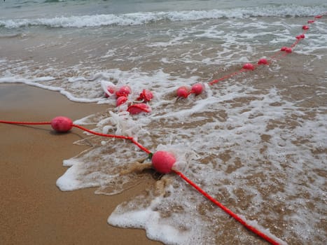 Buoys on a rope in sea water. The lifebuoys are pink restraints to alert people to the depth of the water. Rescue of the drowning. Delimiting a place on a sandy beach between hotels. Wave with bubbles
