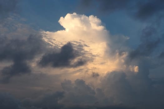 A beautiful cloud illuminated by sun during sunset. Blue sky and dark gray clouds around the edges. Evening sky. Climate change, aviation, hydrometeorology. Cumulus cotton clouds in the stratosphere.