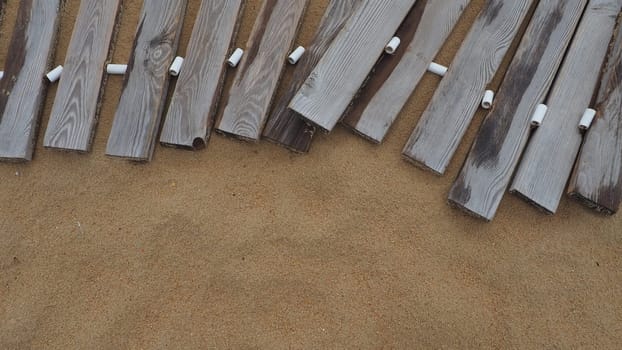 Wooden footbridge on a sandy beach. Uneven, damp wooden planks held together. The edge of the beach season at the hotel. No people, copy space. Equipped sandy beach after a storm or cyclone. Tourism.