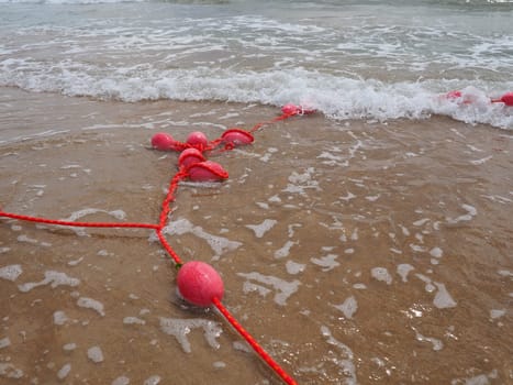 Buoys on a rope near sea water. The lifebuoys are pink restraints to alert people to the depth of the water. Rescue of the drowning. Delimiting a place on a sandy beach between hotels. Wave with bubbles.