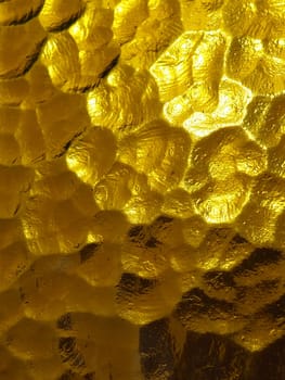 golden yellow corrugated glass with a light and dark background. reflections of light. Corrugated glass, rear light source. Play of glare and reflections on a transparent uneven surface