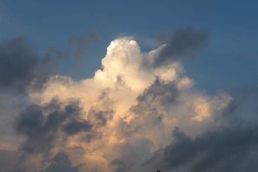 A beautiful cloud illuminated by sun during sunset. Blue sky and dark gray clouds around the edges. Evening sky. Climate change, aviation, hydrometeorology. Cumulus cotton clouds in the stratosphere.