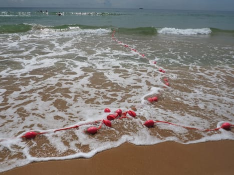 Buoys on a rope in sea water. The lifebuoys are pink restraints to alert people to the depth of the water. Rescue of the drowning. Delimiting a place on a sandy beach between hotels. Wave with bubbles