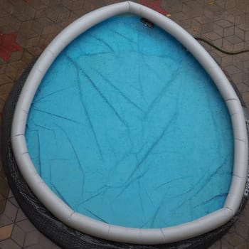 Rubber round pool filled with water. Blue water in the pool. Large drops of rain fall on the surface of the water. Rainy weather at the hotel. No one in the pool due to bad weather.