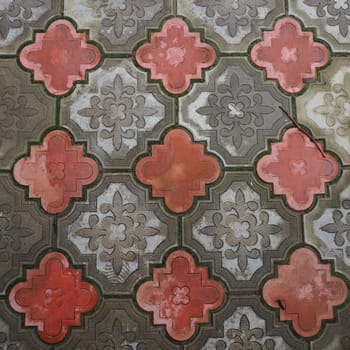 A cobbled street or road lined with square and rounded decorative concrete tiles in gray and red. Stone texture. Geometric east pattern on the floor. Sidewalk, park or pedestrian design option.